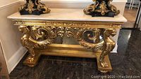 Front view of gold gilt console table showing ornamental scrollwork and marble top
