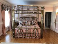 Front view of full brass canopy bed frame with bedding for scale