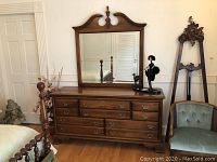 Front view of nine-drawer wooden dresser with matching mirror in room setting.
