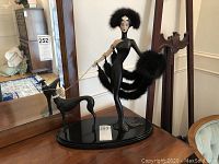 Full view of black Art Deco style Erte doll standing on a black oval base with greyhound figurine on a leash.