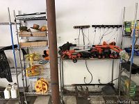 Photo showing Black and Decker cordless yard tools, batteries, chargers on a metal table, extension cord reels and shelves with garden items.