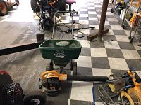 Wide shot of Poulan Pro blower laying on floor next to green Scotts Turf Builder EdgeGuard DLX spreader in a garage or workshop environment.