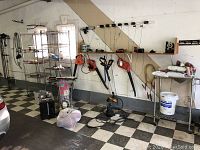 Two metal wire shelving racks in a garage setting with various tools on a pegboard wall behind them and other garage items around them. Both racks have visible rust on the wire shelves and legs.