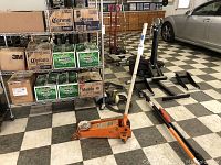 Floor jack placed on tiled floor near shelving and vehicle.