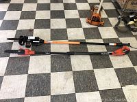 Two electric tree trimmers laid out on black and white checkered floor, one Remington Branch Wizard Plus with pole saw and one Black & Decker trimmer.