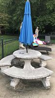 Full setup showing round concrete table, three benches around, closed blue umbrella in center