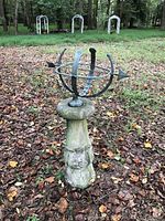 Full view of metal armillary sundial on concrete pedestal in outdoor setting