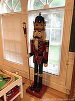 Full height view of 73" wooden nutcracker soldier figure standing in front of window.