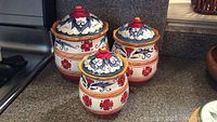 Three hand painted ceramic canisters with decorative floral designs on a kitchen counter.