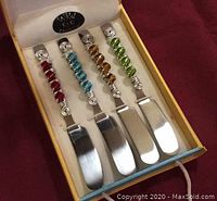 Four appetizer knives with swirl wire and stone bead handles in red, turquoise, amber, and green colors, set inside a yellow box with white interior and Wild Eye Designs logo on the case lid.