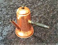 Copper tea pot with ribbed handle and straight spout shown on dark textured surface from angled top view.