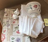 Full view of lot including botanical style oblong tablecloth, white linens, Ansley Bone China sugar and creamer set, and ceramic wall vase.