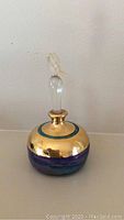 Full view of the signed pottery perfume bottle showing its round shape and gold and blue-purple glaze with frosted glass bird stopper