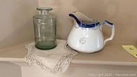 Photo showing apothecary bottle, antique pitcher on crocheted dresser scarf on shelf