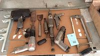Overview of pneumatic tools laid out on cardboard including air hammer, grinder, drill, sander, and saw frame.