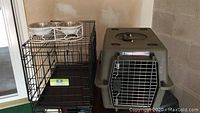 Photo of black wire folding crate, small plastic pet carrier, and elevated double bowl feeding stand