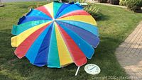 Full overhead image of large multicolor patio umbrella set on grass with outdoor thermometer beside it.