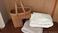 Photo showing the two folded fleece blankets in beige and off-white colors beside a woven basket with handles.