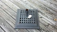 Full photo of matte gray wrought iron patio umbrella stand with square lattice base set on wooden deck. Includes vertical tube for umbrella pole.