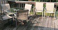 Side view of 42-inch round glass top patio table with six metal frame woven fabric chairs on wooden deck.