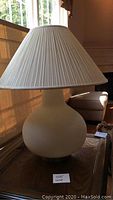 Side view of large white table lamp showing pleated white fabric shade and bulbous round base.
