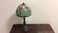 Full view of Tiffany style stained glass lamp showing colorful floral pattern on shade and ornate metal base.