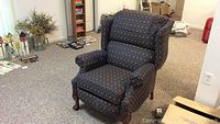 Single recliner chair shown from the front, displaying its traditional navy blue and burgundy patterned upholstery and wood legs.