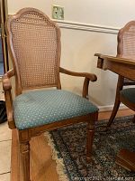 Front view of an armchair showing caned back, wooden frame, padded blue-green seat, and armrests.