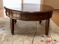 Front view of the round cherry cocktail table showing the drawers on the sides and casters on the legs.