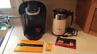 Keurig coffee maker and vintage Corning electric percolator side by side on counter with manuals.