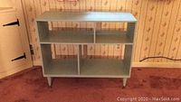 Front view of the light blue Mid Century Modern open bookcase shelf with four compartments and tapered legs.
