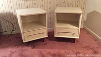 Front view of both white mid century modern night stands showing drawer, open shelf, and tapered metal legs.
