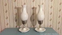 Pair of white hobnail hurricane lamps with hobnail pattern on glass and base, shown unlit.