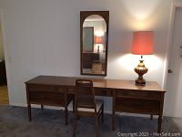 Front view of American of Martinsville vanity desk with chair and lamp on top, mirror mounted on wall above.