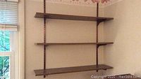 Three adjustable medium brown veneer shelves mounted on vertical metal racks attached to the wall.