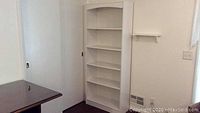 Full view of the white bookcase positioned near a white wall, showing shelving and base.
