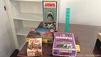 Lot of four vintage games on shelf, including Jaws game, Guinness World Records trivia game, Pit card game, and a blue puzzle piece container on a Big Ben jigsaw puzzle box.