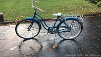 Full side view of teal Schwinn Hollywood bicycle showing double rear wire baskets, rear rack, fenders, and kickstand.