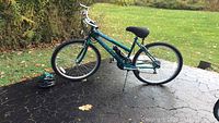 Full side view of green/blue girls Quasar Pacific bicycle, showing frame, tires, kickstand, and helmet on ground