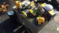 Wide view of various flashlights and floodlights on table outdoors, mostly yellow and black items with batteries and packaging included
