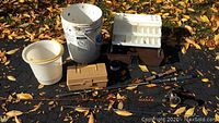 Photo showing three fishing poles, two tackle boxes, and two buckets arranged on ground with fallen leaves.
