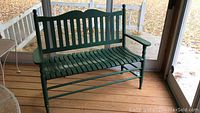 Front view of primitive green painted farmhouse bench showing slatted seat, vertical slat backrest, armrests, and wear on paint.