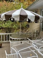 Large round patio table with brown and white striped fabric umbrella and white chairs around it, visible outdoor setting.