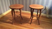 Pair of small round oak tables placed side by side on a hardwood floor against wallpapered wall.