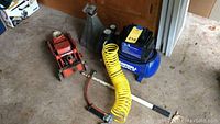 Photo showing orange hydraulic car jack, metal jack stand, blue Campbell Hausfeld air compressor with yellow coiled hose on the floor.