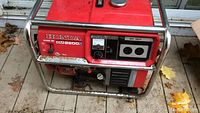 Side view of Honda EM2200X red portable generator showing control panel with outlets, circuit breaker and voltage meter, and steel frame.