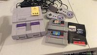 Overview of the Super Nintendo console with two controllers and two game cartridges on white table surface.