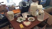 Overview of items on a table including Keurig coffee maker, Juiceman juicer, seasonal decor plates, and coffee accessories.