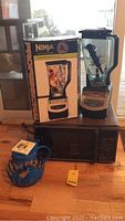 Ninja Professional Blender next to original box, GE microwave and blue microwave popcorn popper all placed on wooden floor.