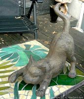 Front-side view of cast iron cat stretching on green tile surface